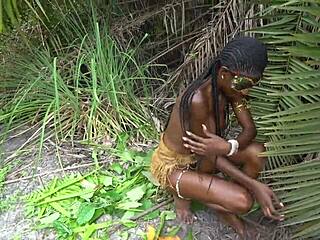African native woman cooks topless in wild jungle setting. Her skinny frame shines under the sun.